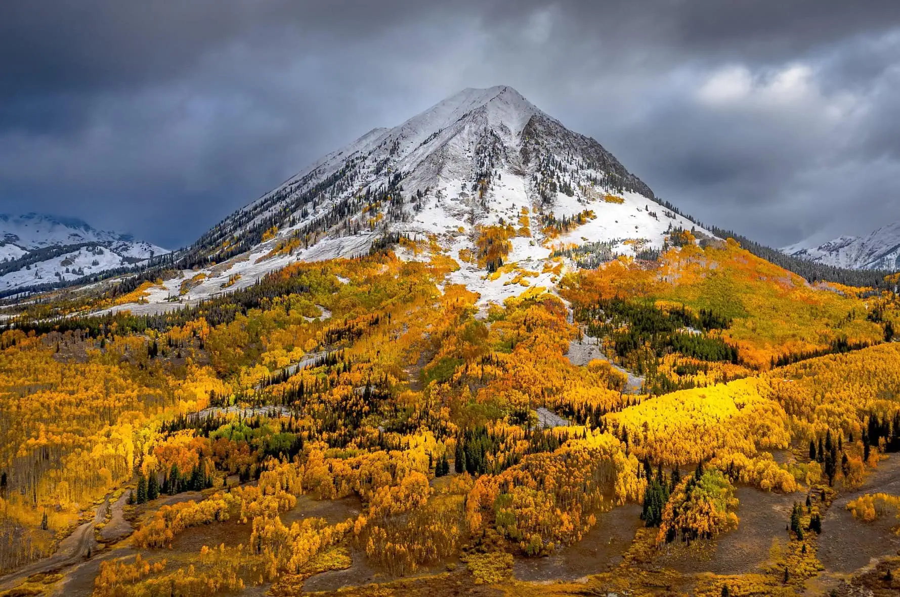 Snow-dusted peak above golden aspens near Crested Butte in fall storm light