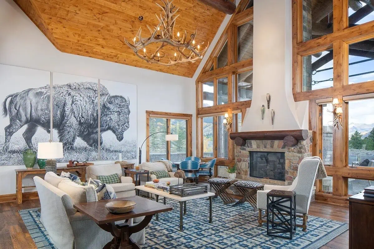 Vaulted living room with wood ceilings, antler chandelier, and panoramic mountain windows
